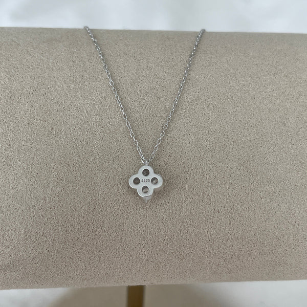 Silver necklace with a clover-shaped pendant on a gray cushion