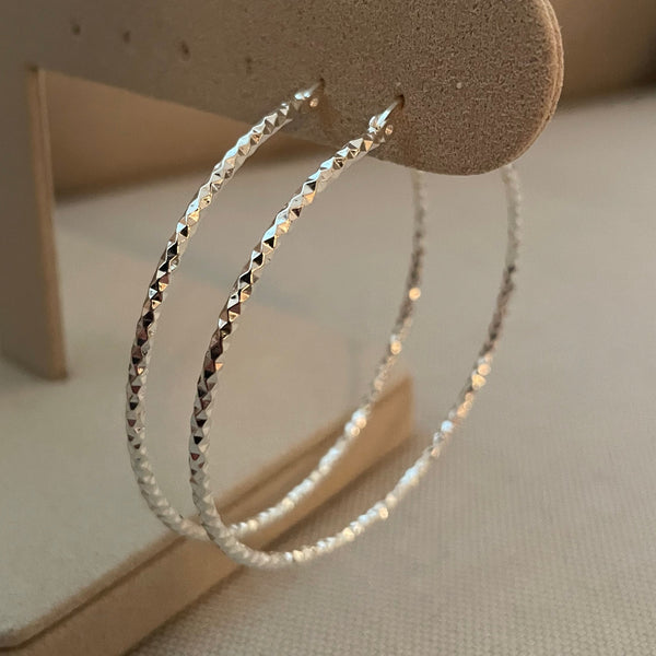 Silver hoop earrings on a beige stand against a neutral background