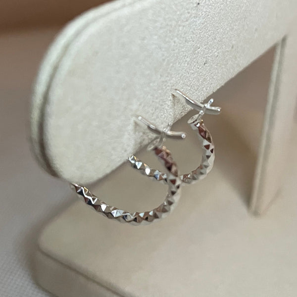 Silver earring on a white cushion with a neutral background
