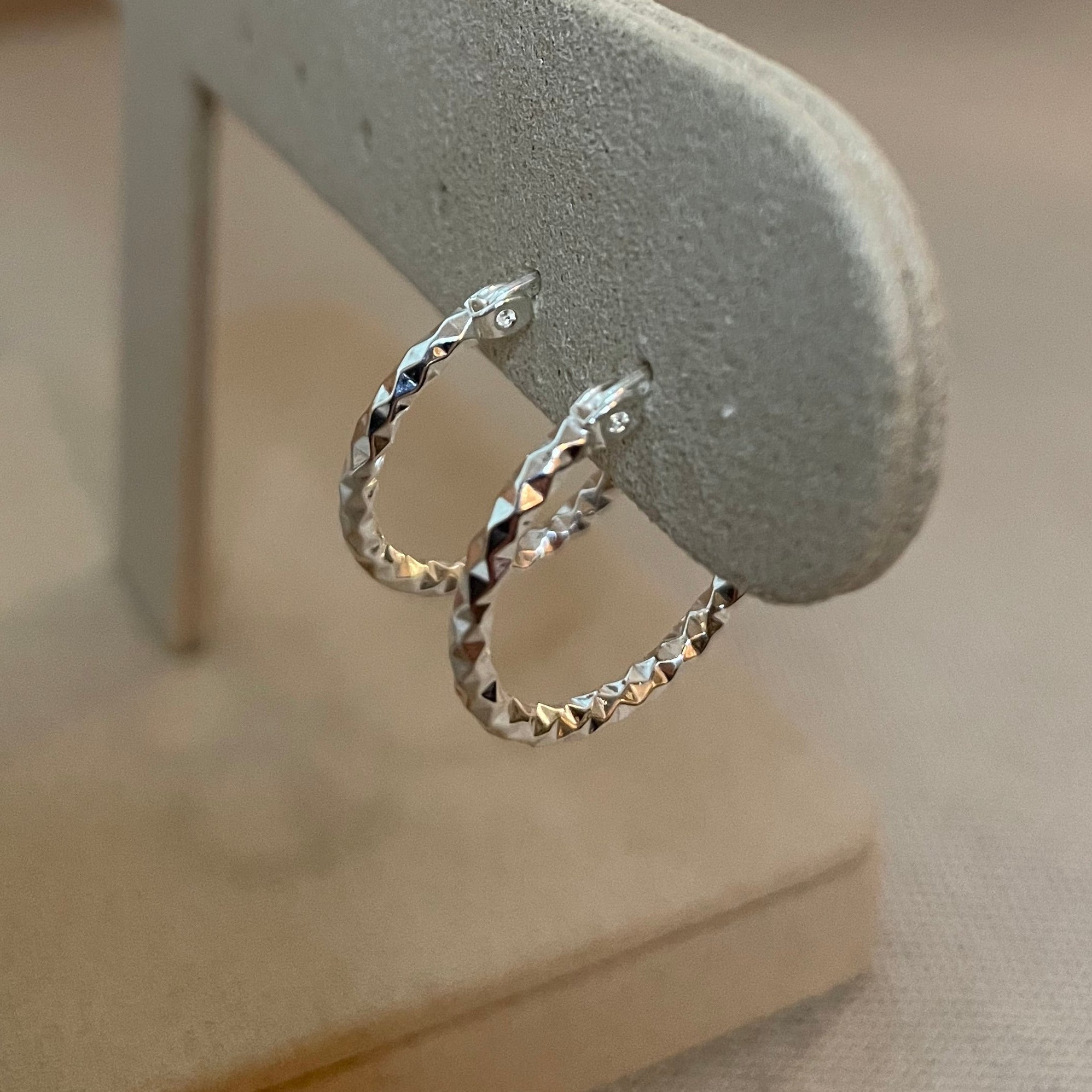 Silver hoop earrings on a gray stand against a neutral background