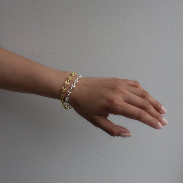 Hand wearing a gold and silver bracelet on a plain background