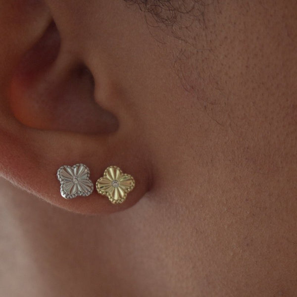 Close-up of a person wearing gold and silver floral earrings.