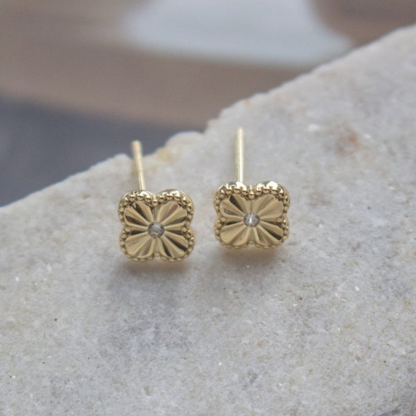 Gold clover earrings with diamond centers on a stone surface