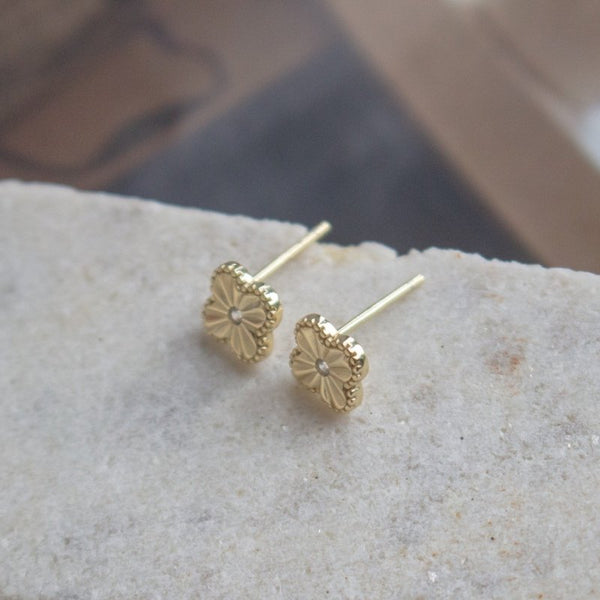 Gold floral earrings on a stone surface