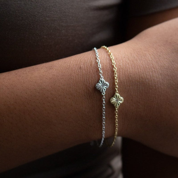 Two delicate bracelets on a wrist against a dark background