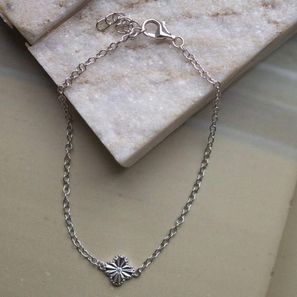 Silver chain bracelet with a clover-shaped clasp on a marble surface