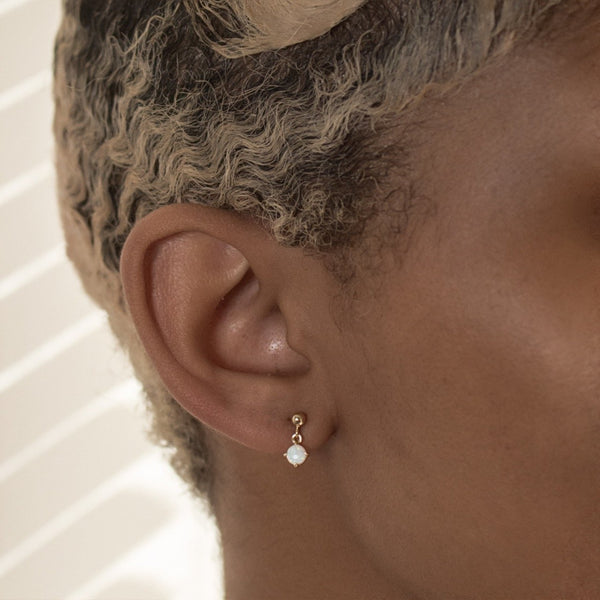Close-up of an ear wearing a gold earring with a small round gemstone.