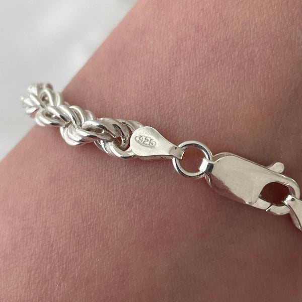 Silver bracelet with a rope design on a wrist against a neutral background