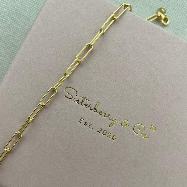 Gold chain bracelet on a pink box with 'Sisterberry & Co' branding.