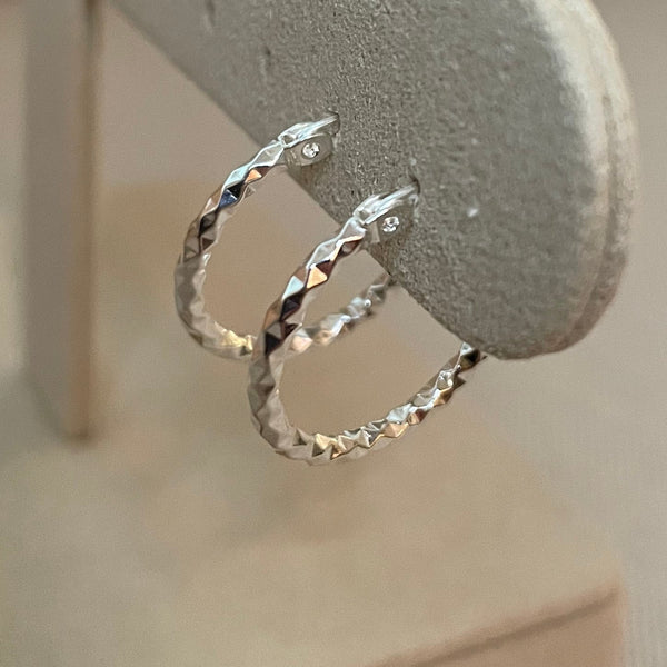 Silver hoop earrings on a gray stand against a neutral background