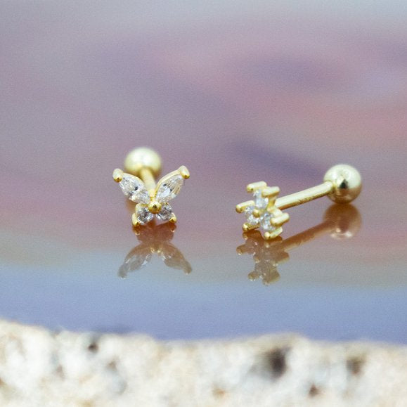 Gold butterfly earrings on a reflective surface with a blurred background