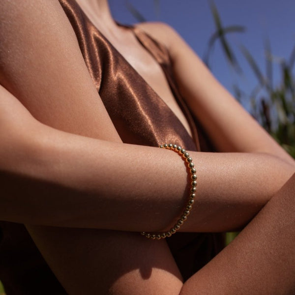 Woman wearing Emma Ball chain bracelet in gold outside in the sun