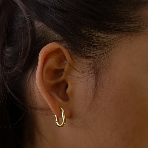 Close-up of an ear wearing a gold hoop earring with dark hair.