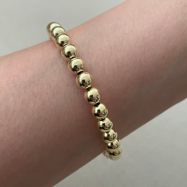 Gold beaded bracelet on a wrist against a neutral background