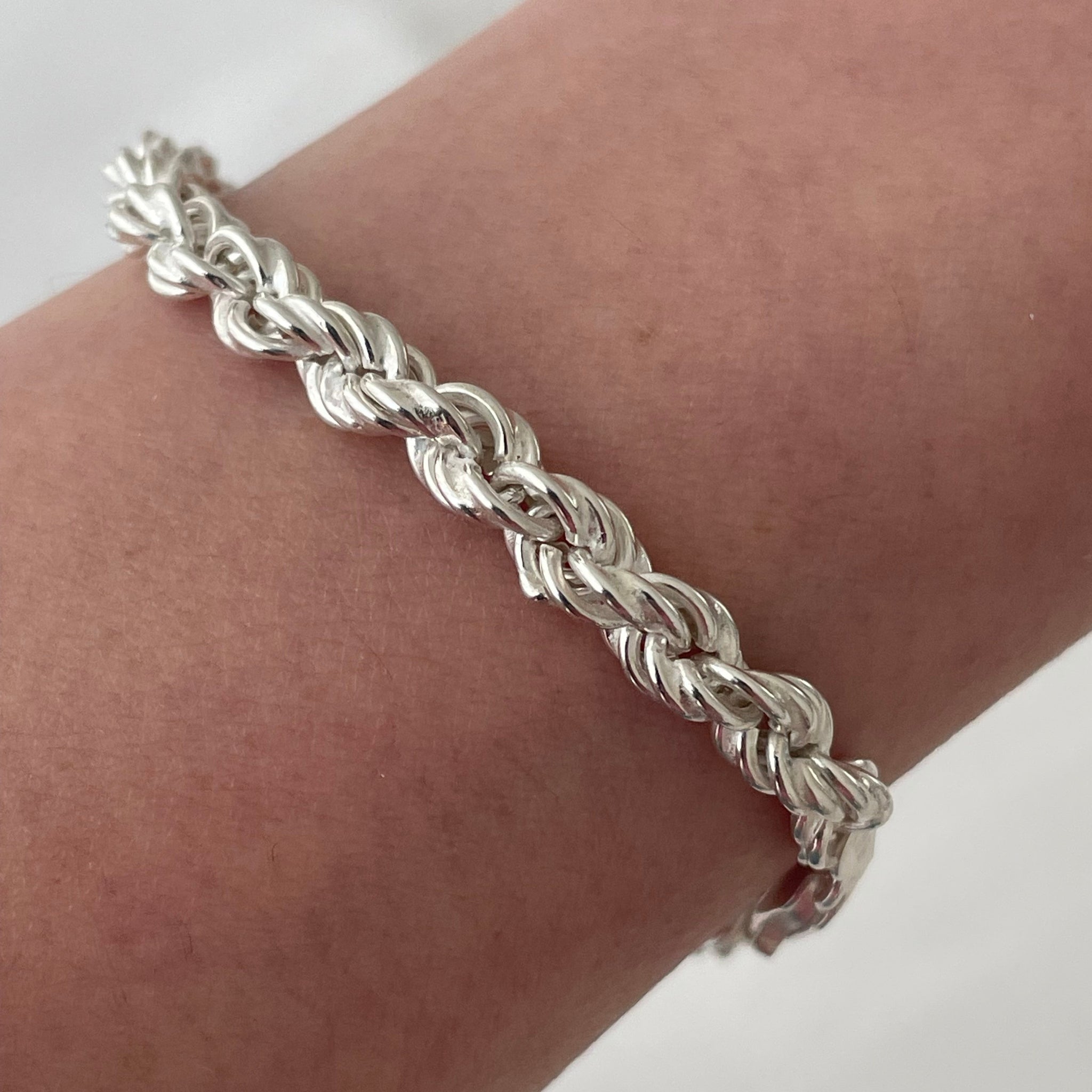 Silver braided bracelet on a wrist with a plain background