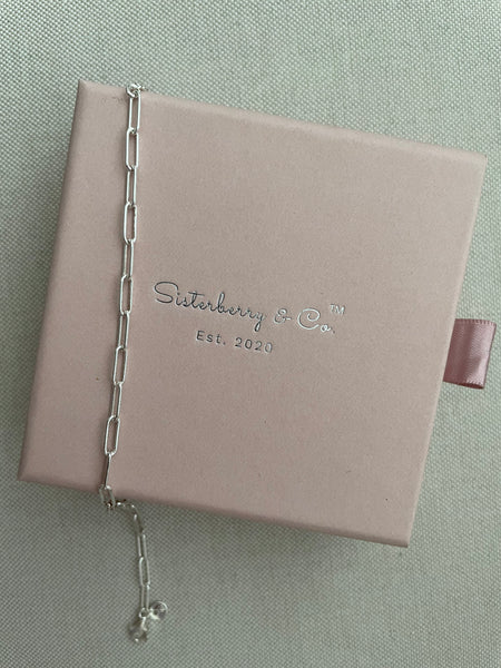 Pink jewelry box with 'Sisterberry & Co' branding and a silver bracelet on a light gray background