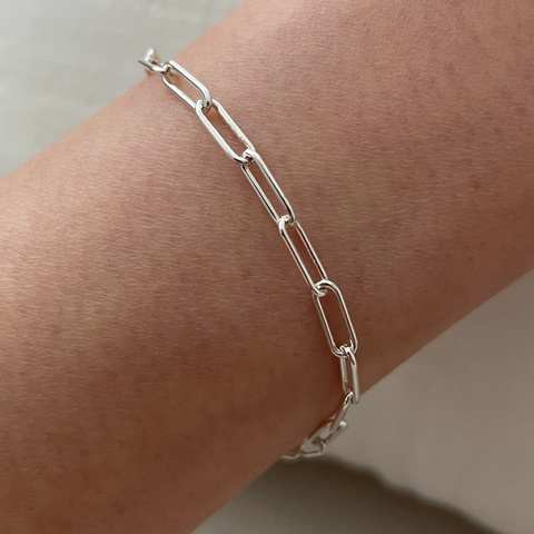 Silver chain bracelet on a wrist against a neutral background