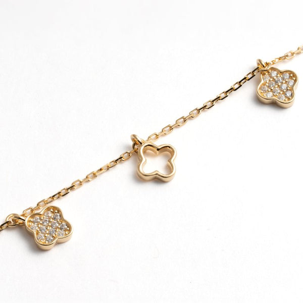 A gold chain bracelet featuring three clover-shaped charms, including two pavé-set clear stones and one openwork clover pendant, on a white background.