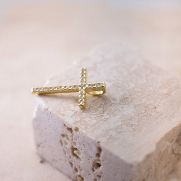 Gold cross pendant with cubic zirconia on a textured beige stone