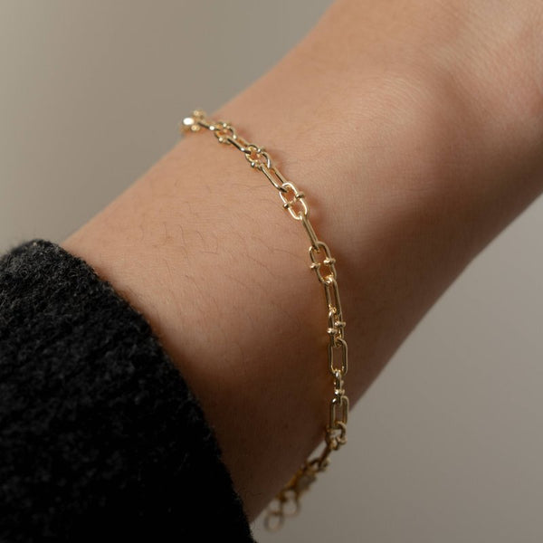 Gold chain bracelet on a wrist with a neutral background