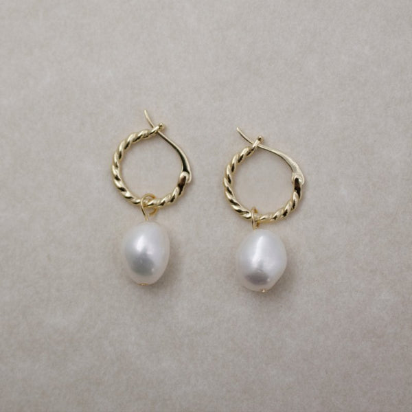 Gold hoop earrings with white pearls on a light gray background