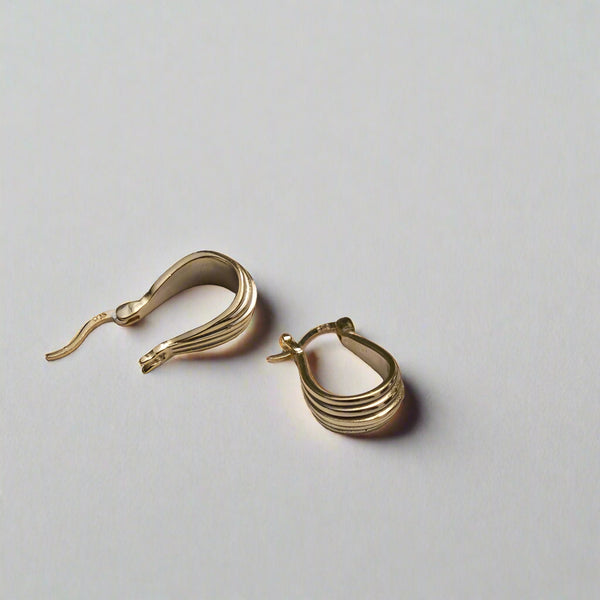 Gold hoop earrings on a light surface with green leaves in the background