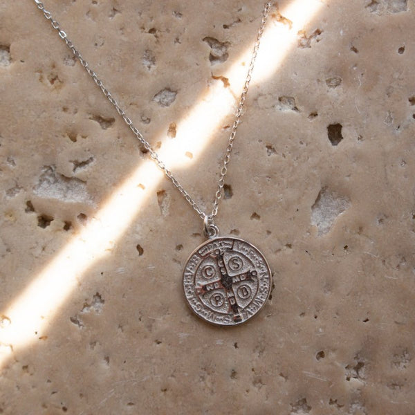 Silver necklace with a peace coin pendant on a textured beige surface