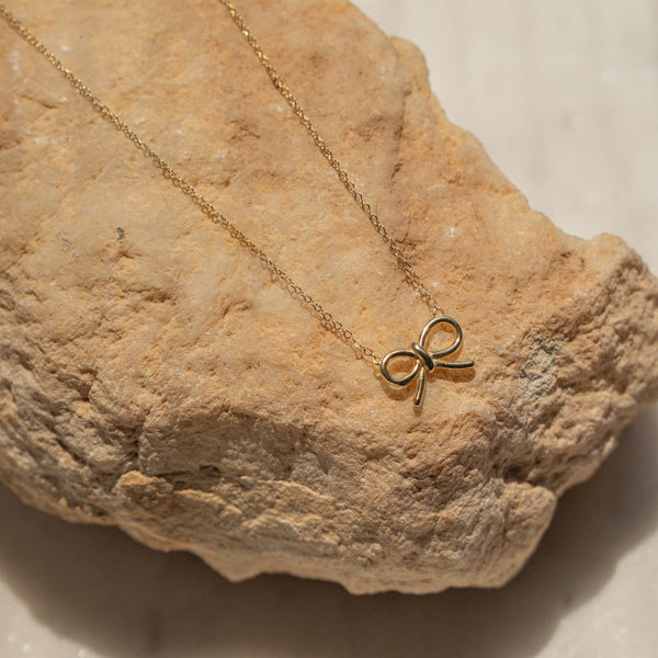Gold bow-shaped necklace on a textured stone surface