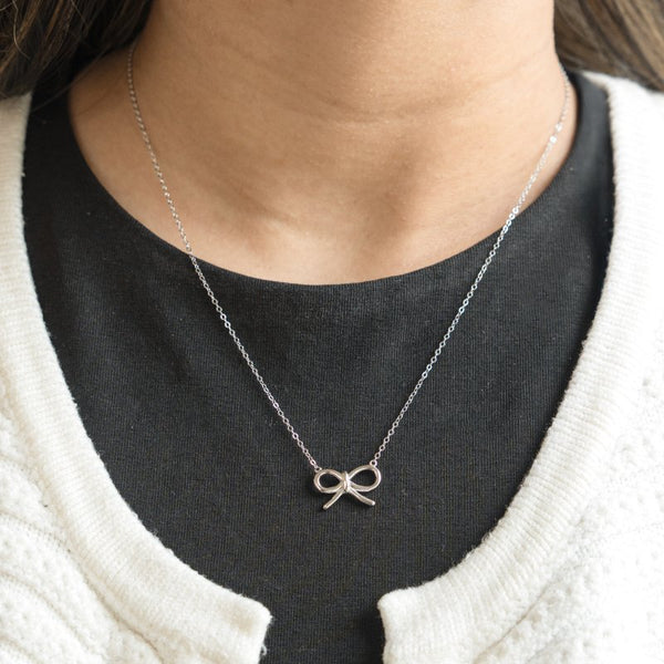 Silver bow necklace worn by a person with a black shirt and white sweater.