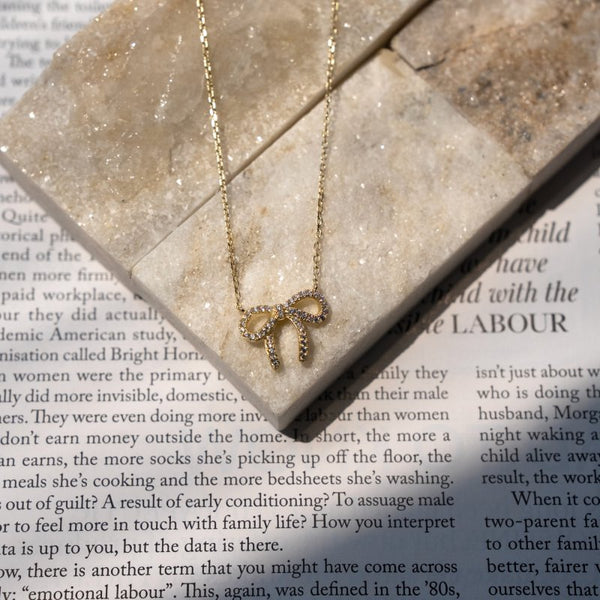 Gold bow-shaped necklace on a textured surface with text underneath