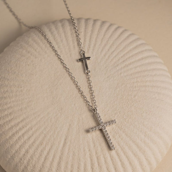 Silver cross necklace on a textured beige surface