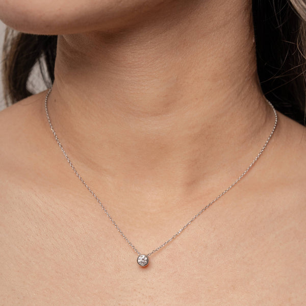 Silver necklace with a small round diamond bezel pendant on a woman