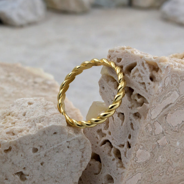 Gold twisted ring on a textured beige surface