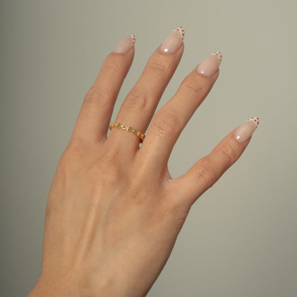Hand with beige nail polish and a gold ring on a plain background