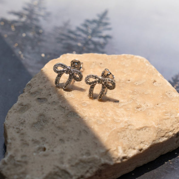 Pair of bow-shaped earrings on a stone surface with a natural background