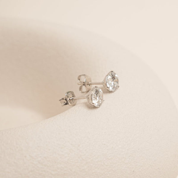Pair of silver earrings with clear gemstones on a beige background