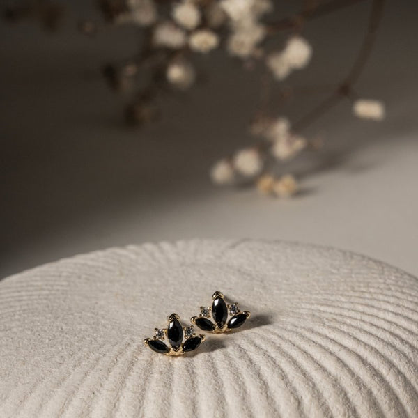 Pair of black and gold earrings on a textured surface with blurred flowers in the background